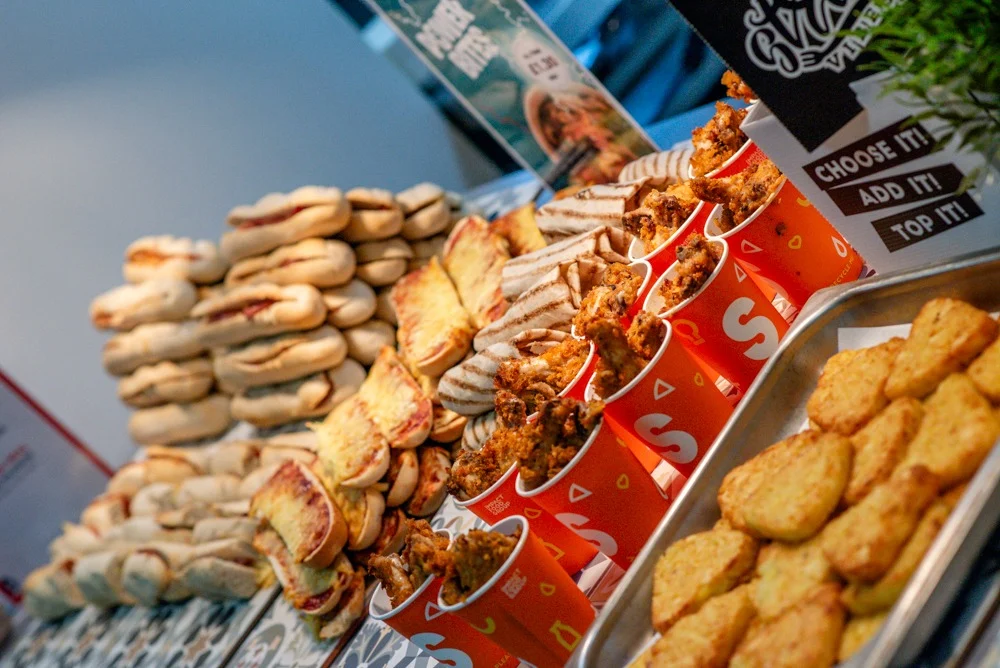 Display of various snacks including roasted nuts, fried chicken in red packaging, and biscuits at a food stall